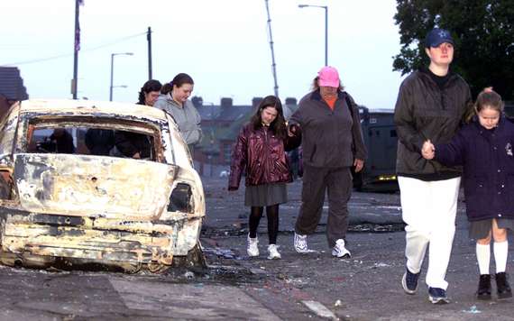 Local residents of the Glenbryn area in North Belfast walk past burnt-out remains of an armored police car following overnight rioting between Nationalists and Loyalists crowds January 10, 2002 in Belfast, Northern Ireland. (Photo By Cathal McNaughton/Getty Images)