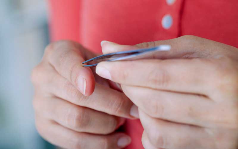 A woman removes a splinter from her finger with tweezers. Credit: BSIP/UIG/Getty Images