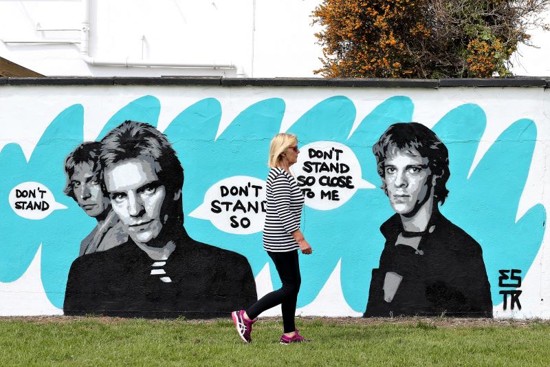 April 28, 2020: Local resident Goretti Harrar passing wall murals featuring figures from popular culture in support of social distancing in Tallaght, Dublin, by artist Emmalene Blake. The mural features Sting and The Police.